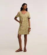 Vestido corto tipo t-shirt color verde oliva con estampado de paisaje tropical en tonos beige. Tiene escote en V y mangas cortas.