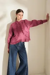 Camisa de lino color morado, con cuello mao, cierre frontal con botones y mangas largas con puños estructurados. Presenta detalles de volados frontales y ruedo con terminaciones desflecadas.