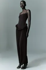 Vestido largo de color negro con escote recto y tirantes finos ajustables. Presenta un diseño con detalle de volados en la cintura que genera un efecto peplum y una falda con caída fluida.