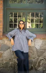 Blusa de algodón con estampado vichy en blanco y negro. Presenta un diseño con frunces en la parte superior del pecho, cuello alto con volado y mangas largas amplias con puños elásticos.