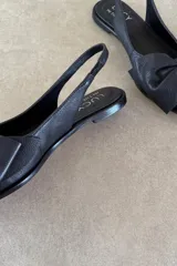 Zapato chatita destalonada de cuero negro, con punta fina y detalle de moño grande en el empeine.