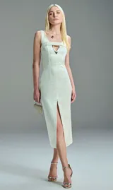 Vestido midi color off white, sin mangas, de corte entallado y silueta estilizada, con escote cuadrado que incluye detalle metálico y tajo frontal en la falda.