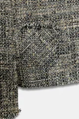 Chaqueta de tweed en tonos gris y negro, con cuello desmontable de pelo sintético marrón, bolsillos delanteros de plastrón y acabados deshilachados.