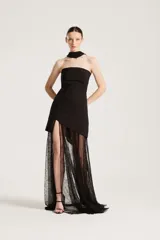 Vestido largo negro de fiesta, con diseño strapless, cuerpo corto entallado y falda larga semitransparente de encaje con abertura lateral pronunciada. Incluye gargantilla a juego.
