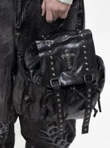 Mochila de cuero sintético negro con acabado texturizado, decorada con tachas metálicas plateadas y un dije de cruz con cadena. Cuenta con cierre de solapa con hebillas, cordón ajustable y bolsillos laterales.