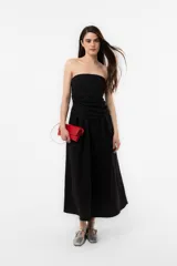 Vestido largo negro con escote strapless, cuerpo fruncido y falda fluida con bolsillos.
