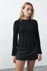 Top de tejido acanalado negro con leve brillo metalizado, de silueta entallada con diseño peplum en la cintura y mangas largas levemente acampanadas.