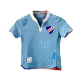 Camiseta de fútbol Umbro del Club Nacional de Football, modelo Away 3 2024 para niños. Diseño celeste con cuello tipo polo con detalles en blanco y rojo. Incluye logo de Umbro, escudo del club y sponsor Antel en el frente.