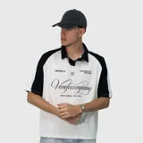 Polo de corte oversize con diseño bicolor, cuerpo en color blanco y mangas raglán en color negro. Presenta cuello tipo polo en negro y estampado gráfico frontal con tipografía cursiva y detalles de la marca.