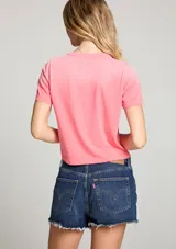 Camiseta corta color rosa con estampado frontal de la frase "Here Comes The Sun" y siluetas de personas caminando.