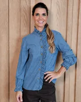 Camisa de denim con cuello alto y volados frontales. Presenta cierre frontal con botones, mangas largas con puños elásticos y detalle de volados en los mismos.