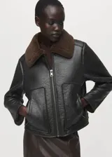 Chaqueta de efecto piel en color negro con diseño oversize, cuello camisero y forro interior de borreguito marrón. Cuenta con cierre delantero con cremallera, bolsillos de parche en los laterales y manga larga.