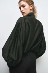 Camisa de corte holgado confeccionada en tejido satinado con mezcla de lyocell. Presenta cuello redondo con escote en pico y lazada frontal integrada. Cuenta con mangas largas abullonadas terminadas en puños anchos y bajo recto.