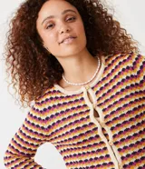 Chaqueta de punto de manga larga, cuello redondo y cierre frontal con botones de madera. Presenta un patrón de rayas horizontales en zigzag con colores crema, mostaza, fucsia y morado.