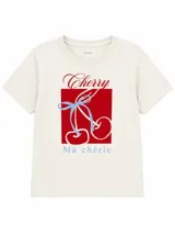 Remera color off-white con cuello redondo y manga corta, de corte clásico. Cuenta con un diseño gráfico central que incluye un cuadrado rojo, la palabra "Cherry" en tipografía cursiva roja, un dibujo de cerezas atadas con un lazo celeste y la frase "Ma chérie" en la parte inferior.