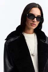 Campera de estilo aviador en color marrón oscuro, con exterior efecto gamuza e interior de corderito sintético color beige. Presenta cuello amplio, cierre frontal con botones y bolsillos laterales.