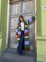 Sacón largo tejido en lana con diseño a rayas horizontales en tonos marrón, verde, blanco y lila. Presenta bolsillos de cuero marrón a la altura de la cadera.