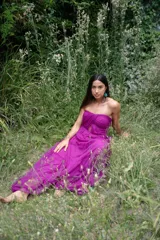 Vestido largo de fiesta color fucsia, sin mangas y con escote strapless. Presenta un corte a la cintura y falda con vuelo. El corpiño tiene un diseño drapeado con abertura en el centro.