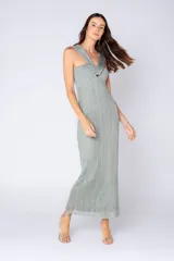 Vestido largo de tejido acanalado con sutil brillo metalizado, color verde menta. Presenta un escote cruzado con un nudo central en el busto y tirantes anchos, con una silueta ajustada en el torso y caída recta.