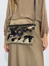 Cartera tipo sobre con lentejuelas doradas y negras reversibles, con borde superior de cuero negro y correa fina de cuero negro.