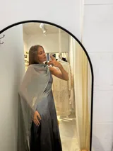 Vestido largo de tafeta con brillo, color verde, de corte al cuerpo y escote asimétrico de un solo hombro. Incluye una pieza de seda liviana drapeada sobre el hombro opuesto.