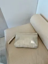 Sobre de mano color plateado con acabado texturizado y cierre superior. Incluye una correa de muñeca personalizada con la marca Rupia y detalles en yute.