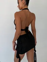 Vestido corto negro con textura arrugada, escote halter profundo y recortes laterales. Presenta un detalle de hebilla metálica dorada en el centro del busto que une las dos partes del corpiño.