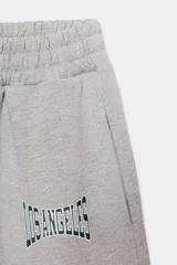Pantalón jogger gris melange de tiro medio con cintura elástica y puños elásticos en los tobillos. Presenta bolsillos laterales ocultos y un estampado frontal con la palabra "LOS ANGELES" en azul marino.