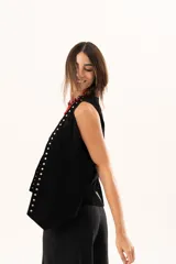 Chaleco oversize de cuero descarne color negro, con diseño de terminación en picos, flecos en la espalda y detalle de tachas metálicas a lo largo de los bordes frontales.