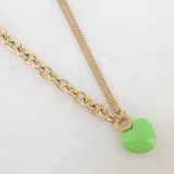 Collar dorado de doble cadena, una de eslabones gruesos y otra fina, con dije de corazón esmaltado color verde.