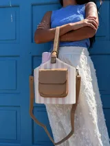 Bolso matero estructurado con diseño a rayas verticales en tonos beige y blanco, cuenta con un bolsillo frontal externo en cuero sintético color tostado, asa de mano corta y correa larga ajustable y desmontable.