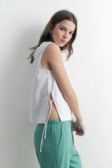Blusa blanca sin mangas confeccionada en lino, con corte recto y aberturas laterales ajustables con lazos.