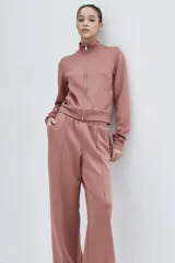 Campera deportiva corta de punto grueso con leve brillo, color rosado, con cuello elevado, cierre frontal y bolsillos laterales insertados.