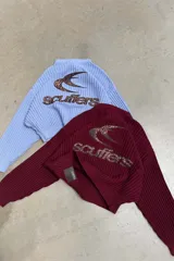 Sweater tejido burdeos de textura acanalada, de corte relajado con cuello redondo, hombros caídos y mangas largas. Cuenta con un gráfico bordado del logo Scuffers en la espalda con estampado de leopardo y terminaciones acanaladas en puños y cintura.