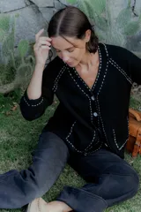 Saco tipo cardigan de punto color blanco con detalles de pespuntes decorativos en color negro a lo largo de los bordes y costuras. Presenta cuello en V, cierre frontal con botones y mangas largas.