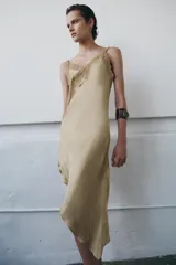 Vestido midi de satén con escote asimétrico y tirantes finos. Presenta una aplicación de encaje a tono en el escote y un bajo asimétrico.
