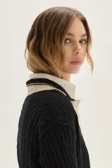 Sweater de punto con diseño de ochos en color crudo, con cuello polo y tapeta de botones en contraste verde. Presenta bordado en el pecho, puños y ruedo acanalados con detalles de rayas en verde.