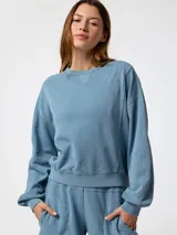 Buzo oversize color celeste de cuello redondo, con mangas largas y puños de rib elástico. Presenta un pequeño logo bordado en el pecho.