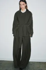 Trench corto de Zara, confeccionado en mezcla de lyocell, color verde militar. Presenta cuello solapa, manga larga con hombro caído y puños con trabilla. Incluye bolsillos delanteros de plastrón, cierre frontal cruzado con botón y cinturón de lazada en el mismo tejido.