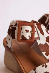 Sandalias planas con diseño de estampado animal print tipo vaca, con puntera cuadrada, tira en T y cierre con hebilla ajustable en el tobillo.