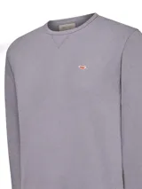 Buzo de cuello redondo confeccionado en algodón orgánico, con diseño clásico de calce regular. Presenta terminaciones en rib en puños, cuello y pretina, e incluye un pequeño parche bordado con el logo de la marca en el pecho.