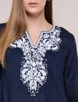 Blusa de corte holgado de inspiración étnica con bordados ornamentales blancos a contraste. Presenta escote en V pronunciado con pechera bordada con motivos arabescos y florales, mangas largas y aberturas laterales en el ruedo.