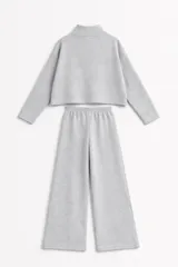 Conjunto de dos piezas en tejido de punto acanalado color gris. Incluye un buzo de corte cropped con cuello alto y cierre frontal, y un pantalón de corte recto con cintura elástica.