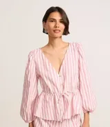 Blusa de tricolina con estampado de rayas verticales en color blanco y rosado. Presenta cuello en V, cierre frontal con botones, mangas 3/4 abullonadas y un lazo ajustable en la cintura.