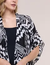 Kimono de gasa ligera negro y blanco con diseño de estampado geométrico, silueta amplia, mangas cortas integradas y ruedo asimétrico con borlas en las puntas.