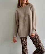 Sweater oversize de tejido liviano, color beige, con cuello redondo, mangas largas con puños acanalados y tajos laterales. Presenta una costura vertical decorativa en el frente y un diseño más largo en la parte posterior.