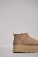 Bota corta tipo botineta en color beige, con diseño de caña baja y plataforma gruesa de goma al tono. Presenta costuras reforzadas y tirador en la parte posterior.