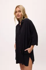 Vestido camisero negro de algodón, con mangas tres cuartos y cuello camisero. Presenta detalles de costura en zigzag color naranja en el cuello y en los puños.