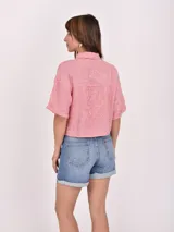 Camisa de corte recto y largo cropped, con estampado de rayas verticales rojas y blancas. Presenta cuello clásico, cierre frontal con botones y mangas cortas con dobladillo.