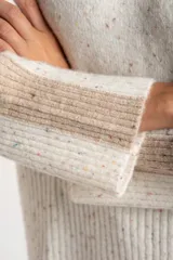 Polera de punto con diseño oversize, cuello alto y mangas largas con paneles laterales en contraste. Presenta un tejido jaspeado con motas multicolores y detalles de lurex.